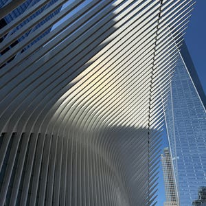 May include: Architectural photograph of a modern building with a white, ribbed, curved facade. The building's design features a series of parallel, curved lines that create a wave-like effect. A blue sky and other skyscrapers are visible in the background.