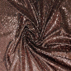 Può includere: Primo piano di un tessuto scintillante con un motivo di piccole paillettes quadrate. Il tessuto è di un colore bronzo intenso, con riflessi che catturano la luce. Le paillettes sono fittamente impacchettate, creando una superficie strutturata.