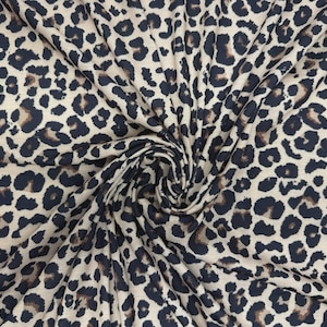 May include: A leopard print fabric. The material features a beige base with dark brown and black spots. The fabric is gathered and swirled, displaying the texture and pattern in detail.