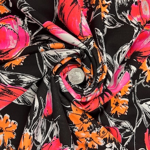 May include: Black fabric with a bold floral design. The pattern showcases large flowers in bright pink, orange, and white, contrasted against a black backdrop. The fabric is gathered, revealing its texture and drape.
