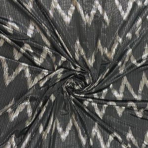 May include: Black fabric with a silver chevron pattern. The fabric is draped and swirled, creating a dynamic display of light and shadow. The chevron design is made up of vertical lines.