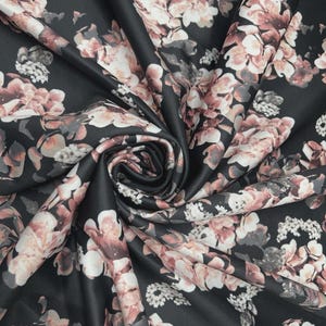 May include: Black fabric with a floral design of blush pink and white flowers with grey accents. The fabric is folded, displaying the detailed pattern and texture. Suitable for clothing or home furnishings.