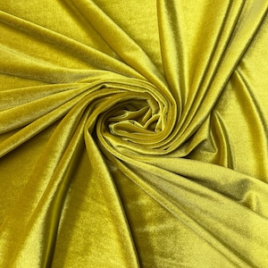 Puede incluir: Primer plano de una tela amarillo dorado vibrante con una textura suave y aterciopelada. El material está drapeado y arremolinado, creando un patrón dinámico de luces y sombras. La tela parece ser un terciopelo lujoso.