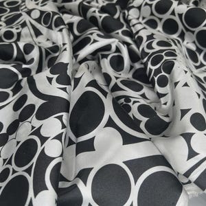 May include: A close-up of a black and white patterned fabric. The design features a repeating pattern of circles and curved shapes. The fabric is draped, highlighting its texture and the flow of the material.