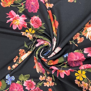 Op de afbeelding: Zwarte stof met een levendig bloemenpatroon. Het ontwerp toont grote, kleurrijke bloemen in roze, oranje, geel en blauw, tegen een donkere achtergrond. De stof is gedrapeerd, wat de textuur en de ingewikkelde bloemenarrangement laat zien.