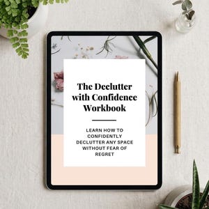 May include: A digital tablet shows a workbook titled "The Declutter with Confidence Workbook." The text on the screen encourages readers to learn how to declutter any space without fear of regret. A gold pen and potted plants are also visible.