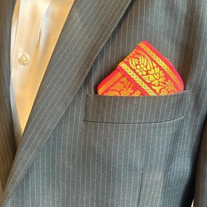 May include: A gray pinstripe suit jacket with a white dress shirt peeking out. A vibrant red and gold patterned pocket square is neatly folded in the breast pocket, adding a pop of color and texture to the formal attire.
