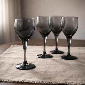 May include: Four gray-tinted wine glasses with long stems are arranged on a beige linen placemat. The glasses have a classic, elegant shape, and the stems are slender. The background is softly lit, creating a sophisticated ambiance.