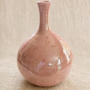 May include: A dusty rose-colored ceramic vase with a bulbous body and a slender neck. The vase has a crackled glaze finish, giving it a vintage appearance. The smooth, rounded shape and soft color make it a decorative item.