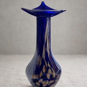 May include: A cobalt blue glass vase with a flared top and a slender neck. The vase features a pattern of tan and white speckles. The vase has a glossy finish and is likely used for decorative purposes.