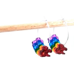 May include: Rainbow colored hoop earrings with a silver metal hoop. The earrings are hanging from a wooden dowel.
