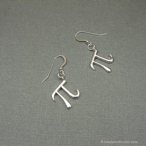 May include: A pair of silver earrings with a pi symbol charm. The earrings are dangle style with a simple hook closure.