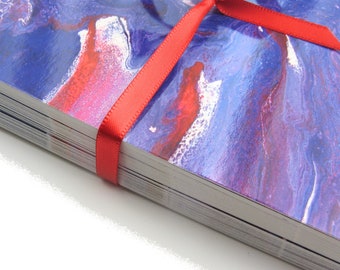 May include: A stack of cards with a blue, red, and white abstract marbled design tied together with a red ribbon.