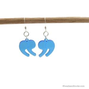 May include: A pair of blue acrylic earrings shaped like quotation marks. The earrings are hanging from silver hooks.
