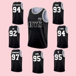 Puede incluir: Camisetas de baloncesto negras con letras y números blancos. Las camisetas muestran los nombres y números de los miembros de BTS: Rap Monster (94), Jin (92), Suga (93), J-Hope (94), Jungkook (97), Jimin (95) y V (95).