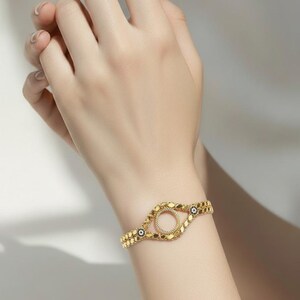 Puede incluir: Una pulsera dorada con un dise&ntilde;o circular central y una banda en forma de cadena. La pulsera presenta peque&ntilde;os elementos decorativos y se lleva en la mu&ntilde;eca. El dise&ntilde;o incluye peque&ntilde;os detalles azules y negros.