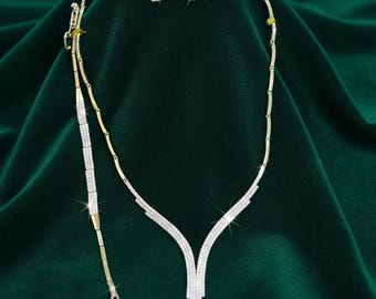 May include: A gold-toned jewelry set featuring a necklace, bracelet, and matching earrings. The necklace and bracelet are adorned with sparkling clear stones. The set is displayed on a dark green velvet surface, creating a luxurious presentation.