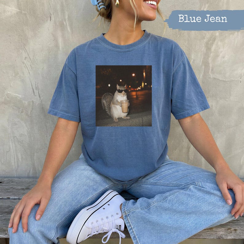 Squirrel wearing sunglasses holding iced coffee, displayed on a blue t-shirt.