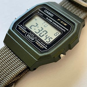May include: A digital Casio F-91W watch with a green case and a gray nylon strap. The watch face displays the time, day, and date. The watch is water-resistant and has an alarm and chronograph functions.