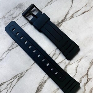Puede incluir: Una correa de reloj de silicona negra compuesta por dos piezas separadas. La pieza m&aacute;s larga presenta una serie de orificios de ajuste rectangulares, mientras que la m&aacute;s corta incluye una hebilla de metal negro y una trabilla de silicona.