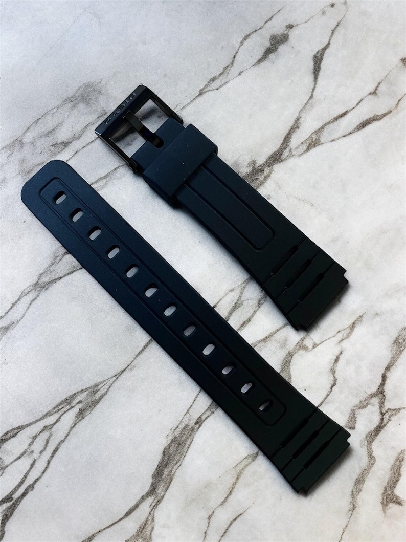 Puede incluir: Una correa de reloj de silicona negra compuesta por dos piezas separadas. La pieza m&aacute;s larga presenta una serie de orificios de ajuste rectangulares, mientras que la m&aacute;s corta incluye una hebilla de metal negro y una trabilla de silicona.