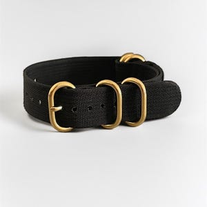 Peut inclure: Bracelet de montre en nylon noir avec des éléments métalliques dorés. Le bracelet présente une texture tissée et plusieurs boucles dorées pour le réglage et la fermeture. Le bracelet est conçu pour la durabilité et une esthétique classique.