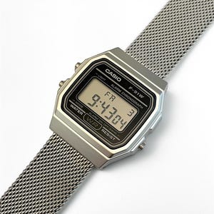 以下が含まれることがあります： メッシュバンドが付いた、シルバーのCasio F-91Wデジタル腕時計。文字盤には9:43:04と表示されています。「CASIO」、「F-91W」、「ALARM CHRONOGRAPH」、「WATER RESIST」、「ALARM ON-OFF/24HR」の文字が印字されています。