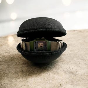May include: A digital watch with a green face and a beige band is displayed inside a black, zippered, spherical case. The watch shows the time. The case is open, revealing the watch.