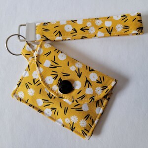 Llavero con forma de minitarjeta con flores blancas sencillas sobre fondo amarillo