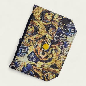 May include: A small, zippered wallet featuring a swirling, colorful design reminiscent of Van Gogh's "Starry Night." The design incorporates images of the iconic blue police box, with a yellow snap closure.