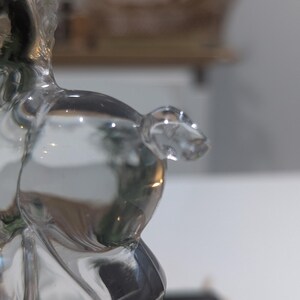 May include: A clear glass figurine of a horse, with a detailed mane and body. The horse is posed in a standing position, with its head slightly turned. The glass is transparent, allowing light to pass through and reflect.