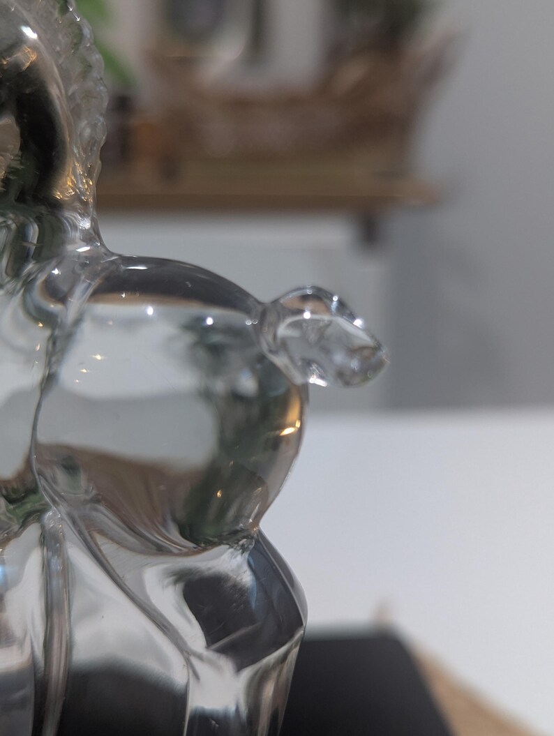 May include: A clear glass figurine of a horse, with a detailed mane and body. The horse is posed in a standing position, with its head slightly turned. The glass is transparent, allowing light to pass through and reflect.