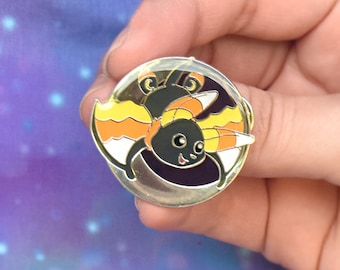May include: A black and orange enamel pin featuring a cartoon bat with candy cane wings. The bat is smiling and has large, round eyes.
