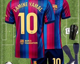 以下が含まれることがあります： 青と赤のストライプのサッカーユニフォーム一式。背中に「LAMINE YAMAL」の名前と「10」の番号が入ったジャージとショーツ。靴下、すね当て、サッカーボールが含まれています。バルセロナチームのロゴが見えます。
