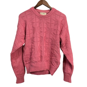 May include: A pink crew neck sweater with a textured geometric pattern. The sweater has long sleeves and ribbed cuffs and hem. The L.L. Bean label is visible at the neckline. The sweater is hanging on a wooden hanger.