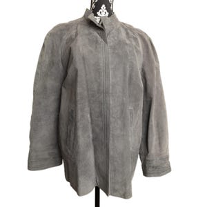 May include: A gray suede jacket with a stand-up collar and long sleeves. The jacket has a button closure and two front pockets. The jacket is displayed on a mannequin.