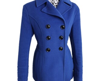 May include: A cobalt blue double-breasted pea coat with six black buttons. The coat has a tailored fit, notched lapels, and long sleeves with decorative cuffs. The coat is displayed on a black and white patterned mannequin.