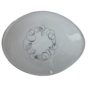 May include: A white, oval-shaped serving dish with a black, abstract swirl design in the center. The dish has a glossy finish and a thin, dark rim. The design is composed of interconnected, looping lines.