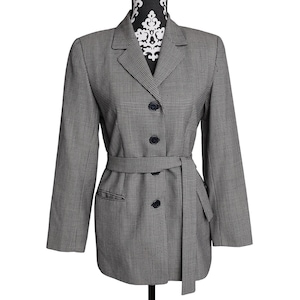 May include: A gray and white houndstooth blazer with a matching belt. The blazer has a notched collar, two front pockets, and three black buttons down the front. The blazer is displayed on a black and white patterned mannequin.