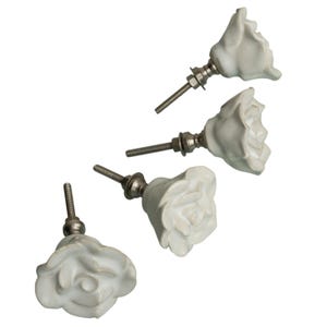 May include: Four white ceramic rose-shaped cabinet knobs with silver-toned hardware. The knobs are arranged diagonally against a white background, showcasing their detailed floral design. These decorative knobs are suitable for furniture and home decor projects.