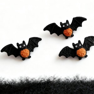 May include: Three handmade Halloween bat decorations. Each bat has black wings and a round orange body. The bats have small white eyes and are arranged on a white background. The bats are made of felt.