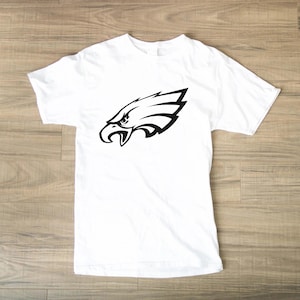 Pode incluir: Camiseta branca com um gr&aacute;fico preto da cabe&ccedil;a de uma &aacute;guia. O desenho da &aacute;guia &eacute; uma imagem estilizada com linhas n&iacute;tidas e um olho detalhado, contrastando com o tecido branco da camiseta.
