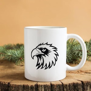 Pode incluir: Caneca de cer&acirc;mica branca com um desenho de cabe&ccedil;a de &aacute;guia preta. O gr&aacute;fico da &aacute;guia &eacute; uma ilustra&ccedil;&atilde;o detalhada com linhas n&iacute;tidas e um olhar focado. A caneca tem uma al&ccedil;a curva.