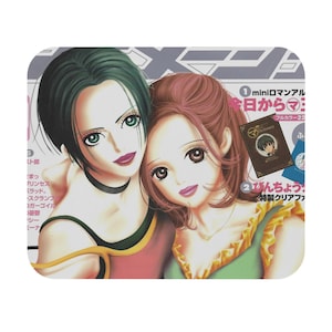 May include: A rectangular mousepad featuring a manga-style illustration of two women. One has green hair and a black choker, the other has brown hair. The image has Japanese text and a small book graphic.