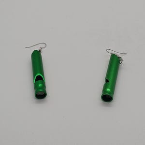 May include: Two green whistle earrings with silver-colored ear wires are displayed against a white background. The earrings are cylindrical with a whistle opening and a rounded bottom. The earrings are made of a shiny, metallic material.