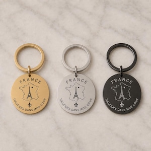 Può includere: Tre portachiavi circolari in metallo nei toni dell'oro, dell'argento e del nero. Ognuno presenta l'incisione del contorno della Francia, della Torre Eiffel, di un piccolo cuore e il testo "FRANCE" e "TOUJOURS DANS MON CŒUR" con un giglio.