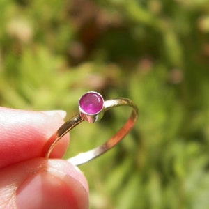 May include: A simple gold band ring with a single round pink gemstone.