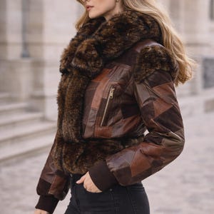 May include: Brown leather jacket with a patchwork design and a faux fur collar. The jacket has a zipper closure and ribbed cuffs. The model is wearing black jeans and carrying a black handbag. A stylish outerwear piece.