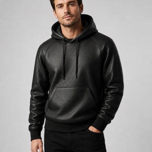 May include: A black long-sleeve hooded sweatshirt featuring a textured leather-like finish, a front kangaroo pocket, and black ribbed cuffs at the sleeves and hem. The hoodie includes matching black drawstrings at the neckline for an adjustable fit.