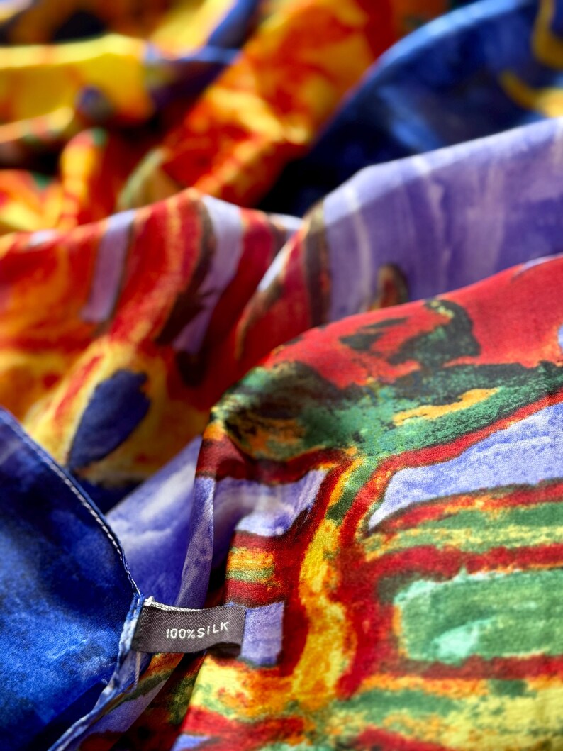 May include: Close-up of a colorful silk scarf with abstract patterns in shades of red, blue, yellow, and purple. The scarf has a tag that reads "100% Silk". The fabric is soft and flowing.